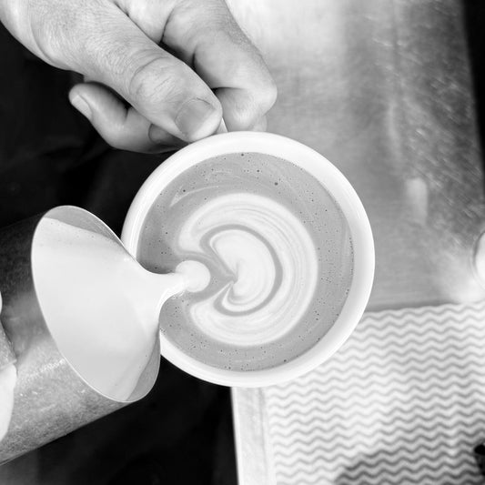 Close-up of a barista pouring steamed milk into espresso to create latte art